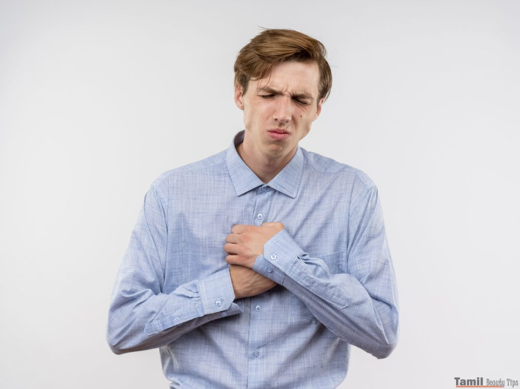 young man blue shirt holding hnads chest looking unwell feeling pain standing white wall scaled 1